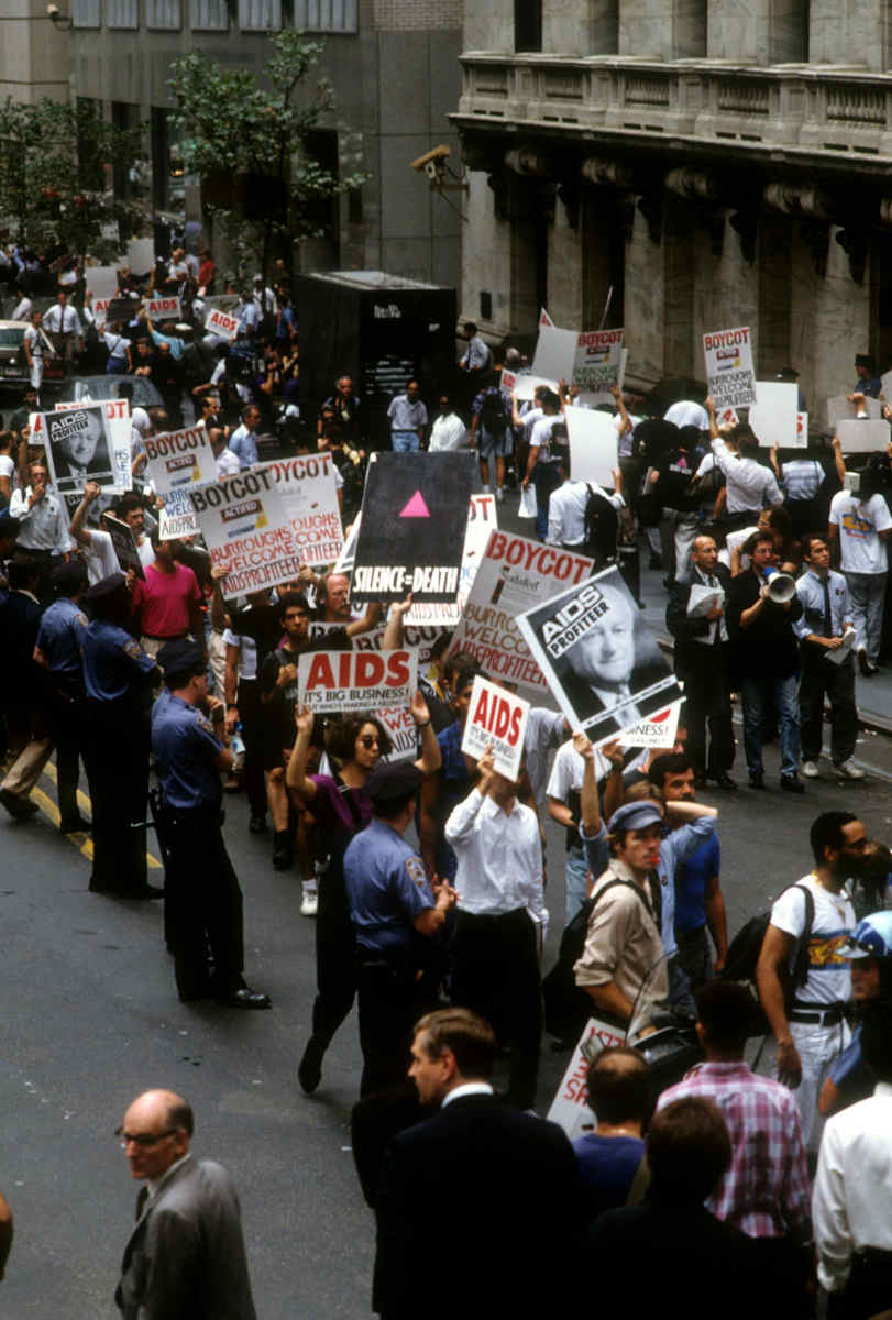 Color photo of demonstrators outside of the New York Stock Exchange with posters. Police stand nearby.