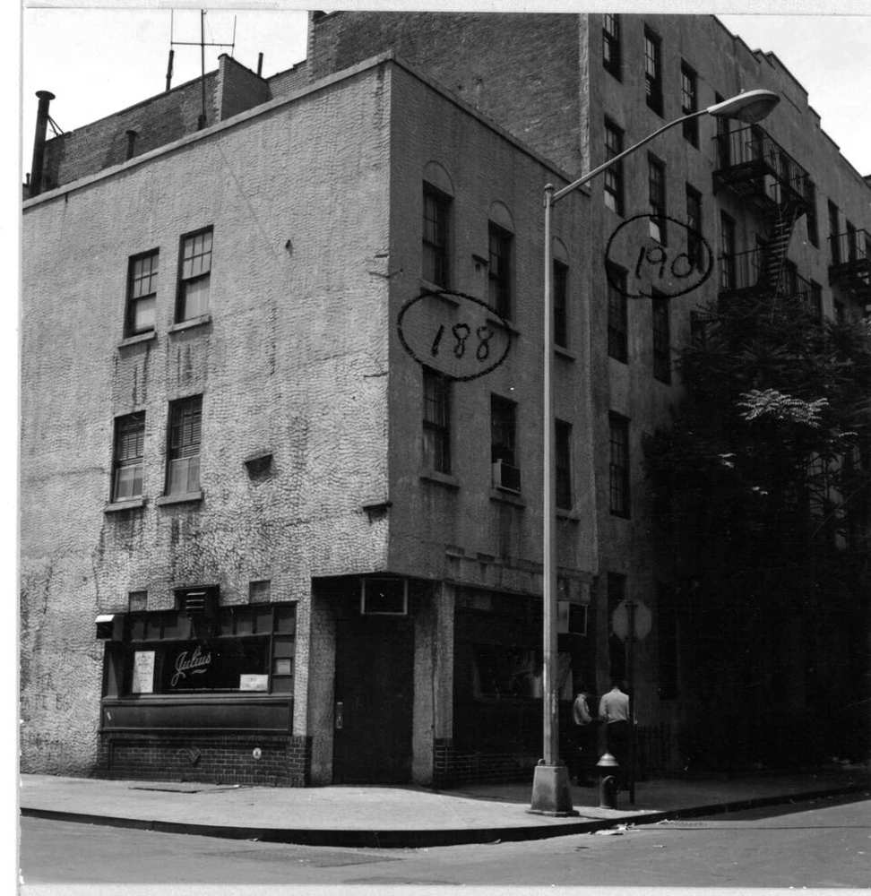 Black and white image of street corner with modest three story brick building. A storefront entrance is at the corner with six-over-one windows above.