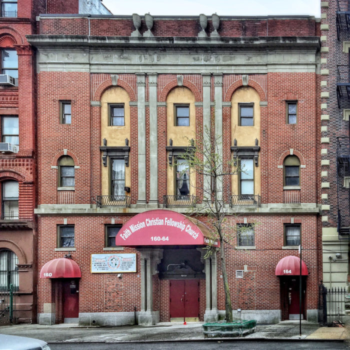 Four story brick building on city street. Concrete pilasters in the front with some yellow plaster accents around the six central windows. A large red awning is above the red door with the name 