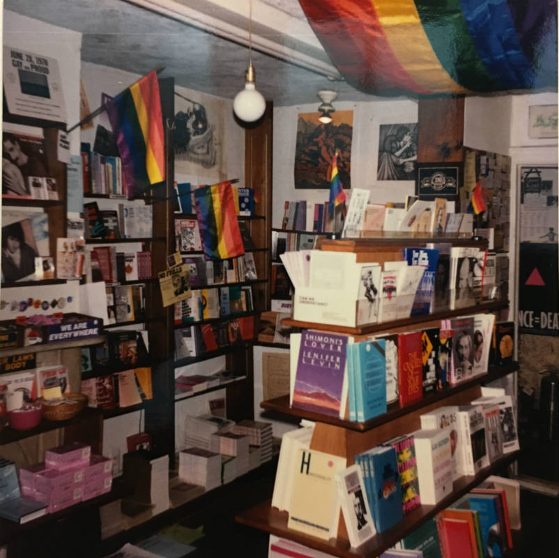 Room with bookshelves. Rainbow flags are attached to the bookshelves and also the ceiling.